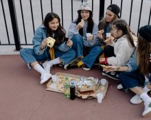 Group of young women enjoying an outdoor picnic with pizza and drinks. Casual and lively scene.