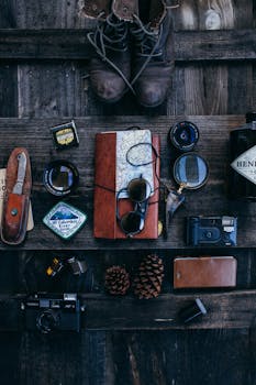 Top view of diary with map placed near retro photo cameras with lenses on surface with magnifying glass and old fashioned boots