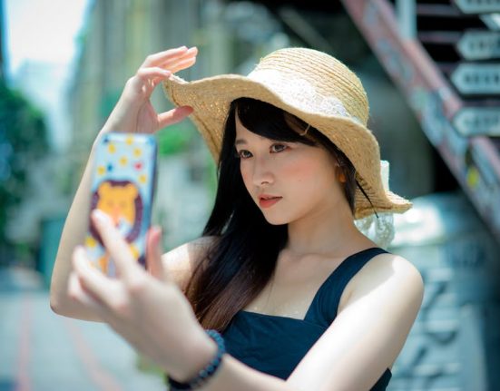 Beautiful Asian woman in a straw hat taking a selfie on a sunny street in Taipei's Xinyi District.