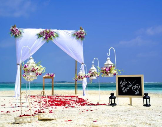 Stunning beach wedding arrangement with floral decor and lanterns on a sunny day.